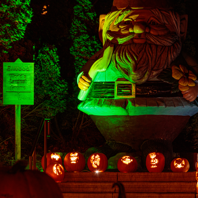 Elwood the Concrete Gnome lit in spooky green lights with jack-o-lanterns at his feet.